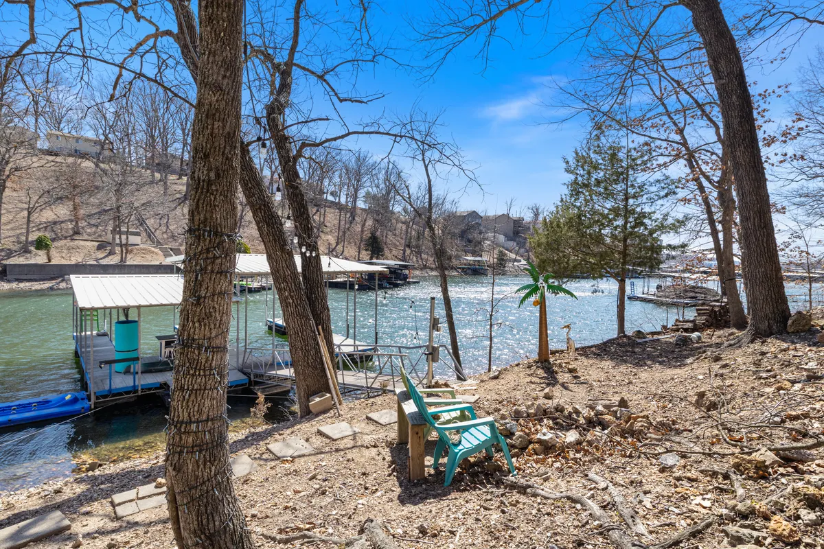 This image showcases a serene lakeside view with boats in the water, a seating area under the trees, and a peaceful atmosphere. The perspective captures the expanse of the lake, inviting guests to imagine boating, fishing, or simply relaxing by the water's edge. The setting sun adds to the tranquil mood, emphasizing the appeal of sunset fishing or evening socials.