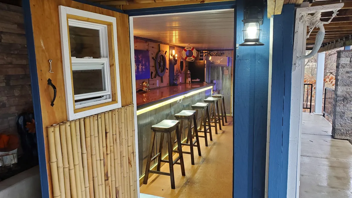 A casual and stylish bar area featuring a bar counter with stools, warm lighting, and decorative wall art. The setup feels inviting and ideal for socializing, casual drinks, or celebrating after a meal.