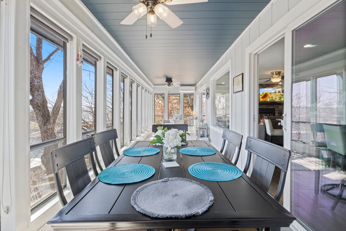 An expansive dining area with a long table set for a group, colorful place settings, and large windows that flood the space with natural light. The windows offer views of the outdoors, hinting at lake vistas and enhancing the social ambiance.