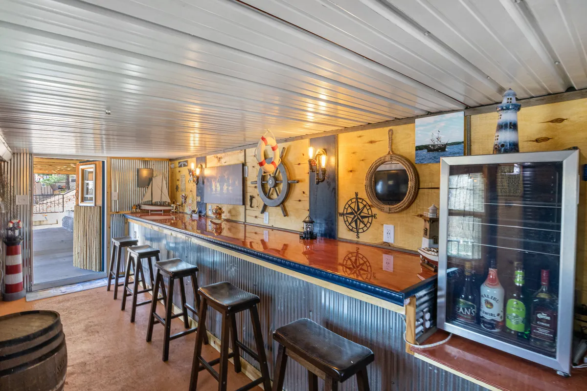 This image captures a stylish bar counter adorned with nautical décor, accompanied by bar stools and a beverage fridge. The relaxed setup is perfect for gatherings and casual drinks, inviting guests to enjoy lively conversations and celebratory events.