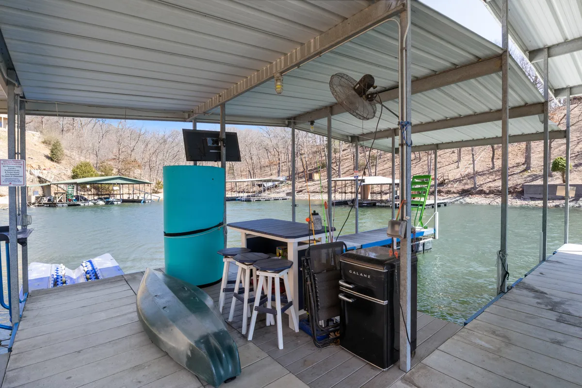 The hero image captures an inviting lakeside setup with kayaks ready for adventure, an outdoor table and chairs perfect for group gatherings, a handy small refrigerator and cooler for refreshments, and a TV for outdoor entertainment. The scene is set against the backdrop of serene waters under a glowing sunset, evoking both relaxation and fun by the lake.