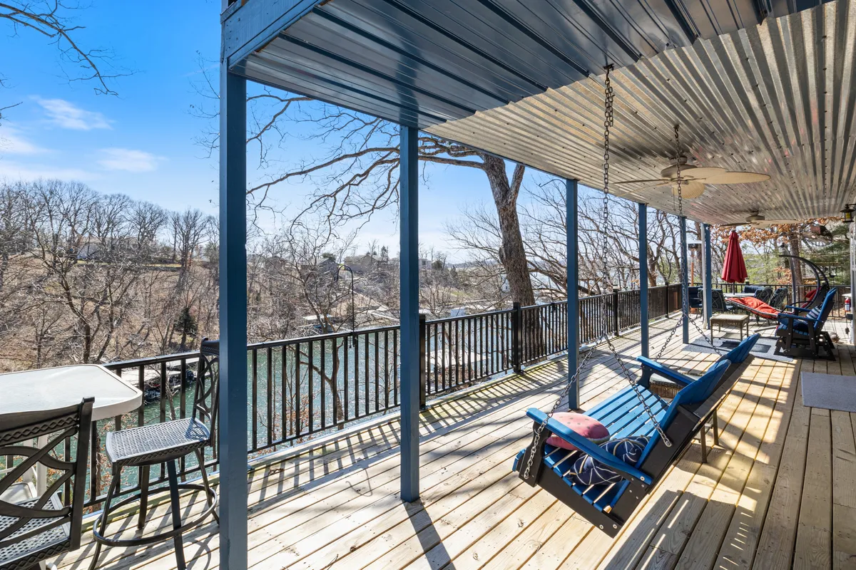 An expansive porch with comfortable outdoor seating, ceiling fan, and direct views over the river, surrounded by trees. The ambiance is serene, inviting guests to relax, socialize, or enjoy meals while taking in the scenic landscape.