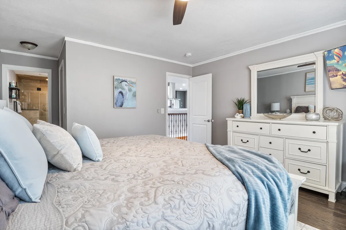 A tranquil bedroom with a comfortable bed featuring decorative pillows, a dresser with a mirror, and soothing artwork on the wall. Natural light flows in, creating a peaceful ambiance ideal for unwinding after a long day or enjoying a quiet morning coffee.