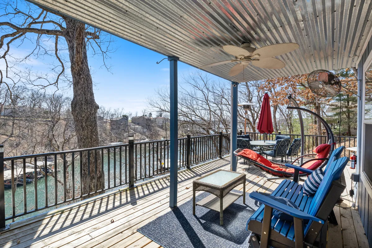 An inviting wooden deck furnished with a hanging chair, blue chairs, a red umbrella, and a table—set against a scenic backdrop. This outdoor space is perfect for morning coffee, reading, or relaxing while enjoying lakefront views.