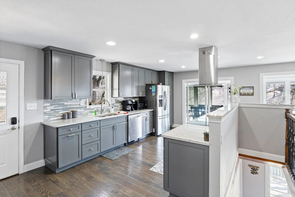 A bright, fully equipped kitchen featuring granite countertops, stainless steel appliances, a central kitchen island, and stylish cabinetry. The inviting space is clearly designed for group cooking and socializing, with plenty of room for meal prep and gathering.