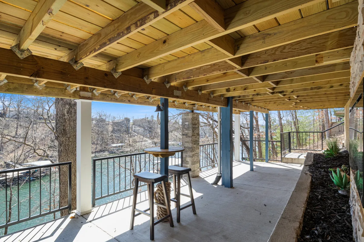 A serene exterior scene featuring wooden beams, bar stools, and railings on a deck overlooking the river. The setup is clearly designed for relaxing with a drink, enjoying nature, or socializing with a group. The view is open, inviting, and ideal for stargazing or watching wildlife by the river.