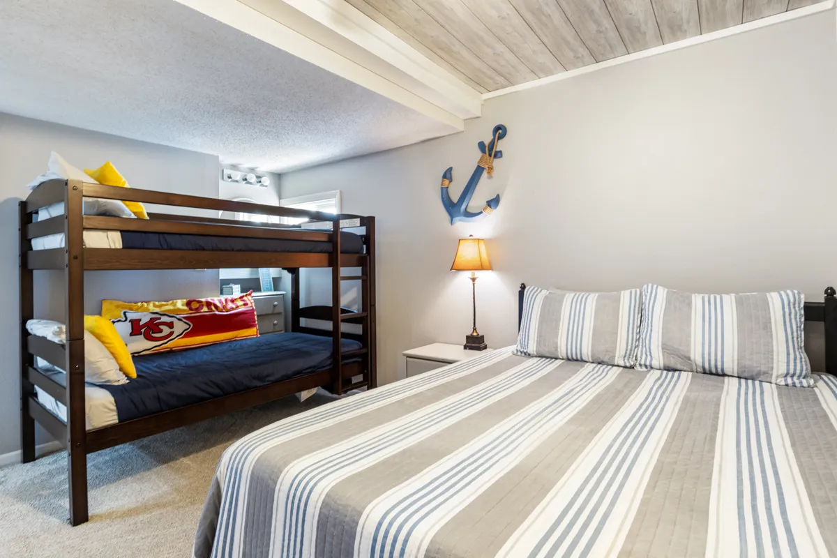 A family-friendly bedroom with both bunk beds and a double bed, accented with nautical-themed decor, a lamp, and playful touches. The space looks warm, cozy, and ideal for families or groups needing flexible sleeping arrangements.