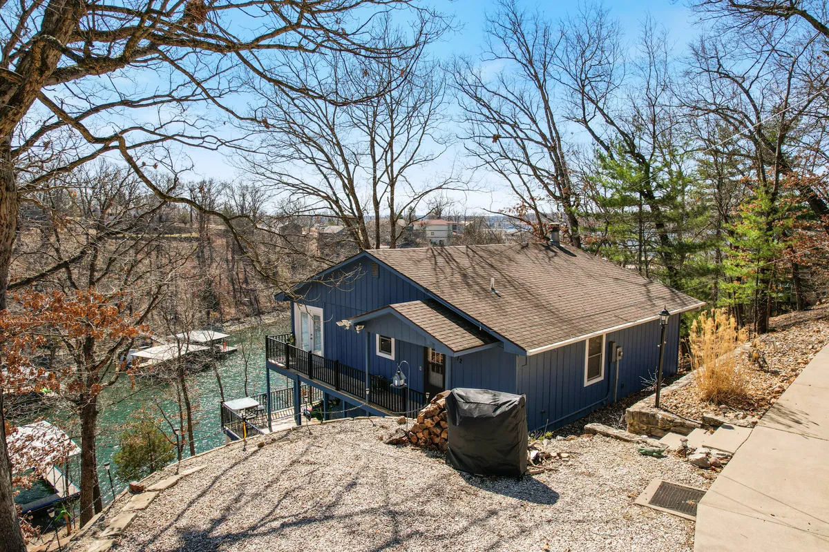 This image features a peaceful lake view with a blue house nestled among surrounding trees and a gravel path that leads to the waterfront. The landscape evokes a sense of tranquility and connection to nature, perfect for groups seeking scenic exploration and outdoor activities.