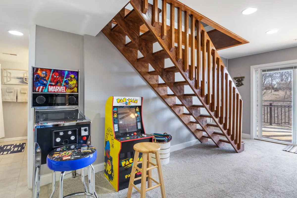 A lower-level space featuring a staircase, arcade machines, and a sliding glass door leading outdoors. This layout blends entertainment and direct access to the deck, hinting at seamless indoor-outdoor transitions.