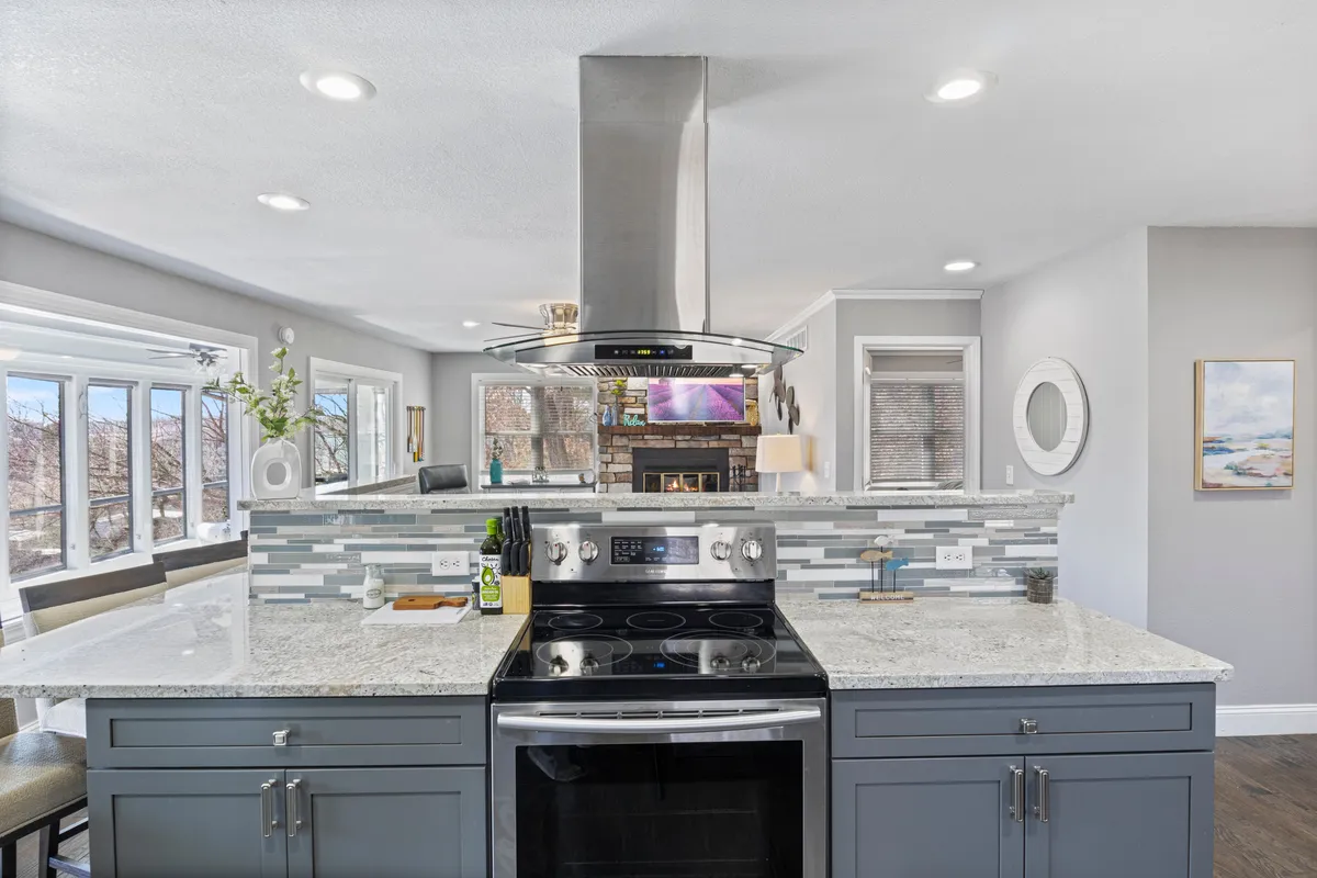 A modern, open-plan kitchen with a central island, stainless steel appliances, tiled backsplash, and large windows that let in plenty of natural light. The layout encourages conversation and group cooking, with plenty of space for multiple people to prepare meals together.